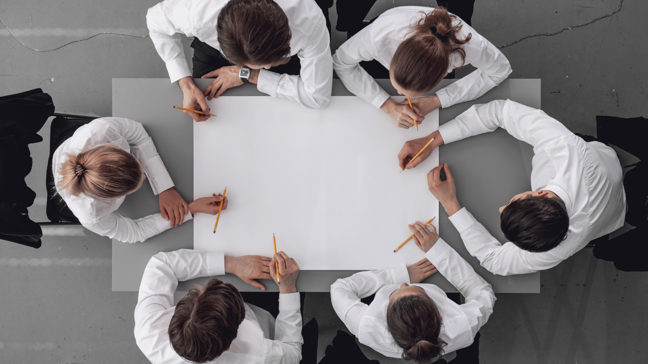 Gruppe von Menschen sitzt gemeinsam an einem Tisch und arbeitet in einer modernen Umgebung.