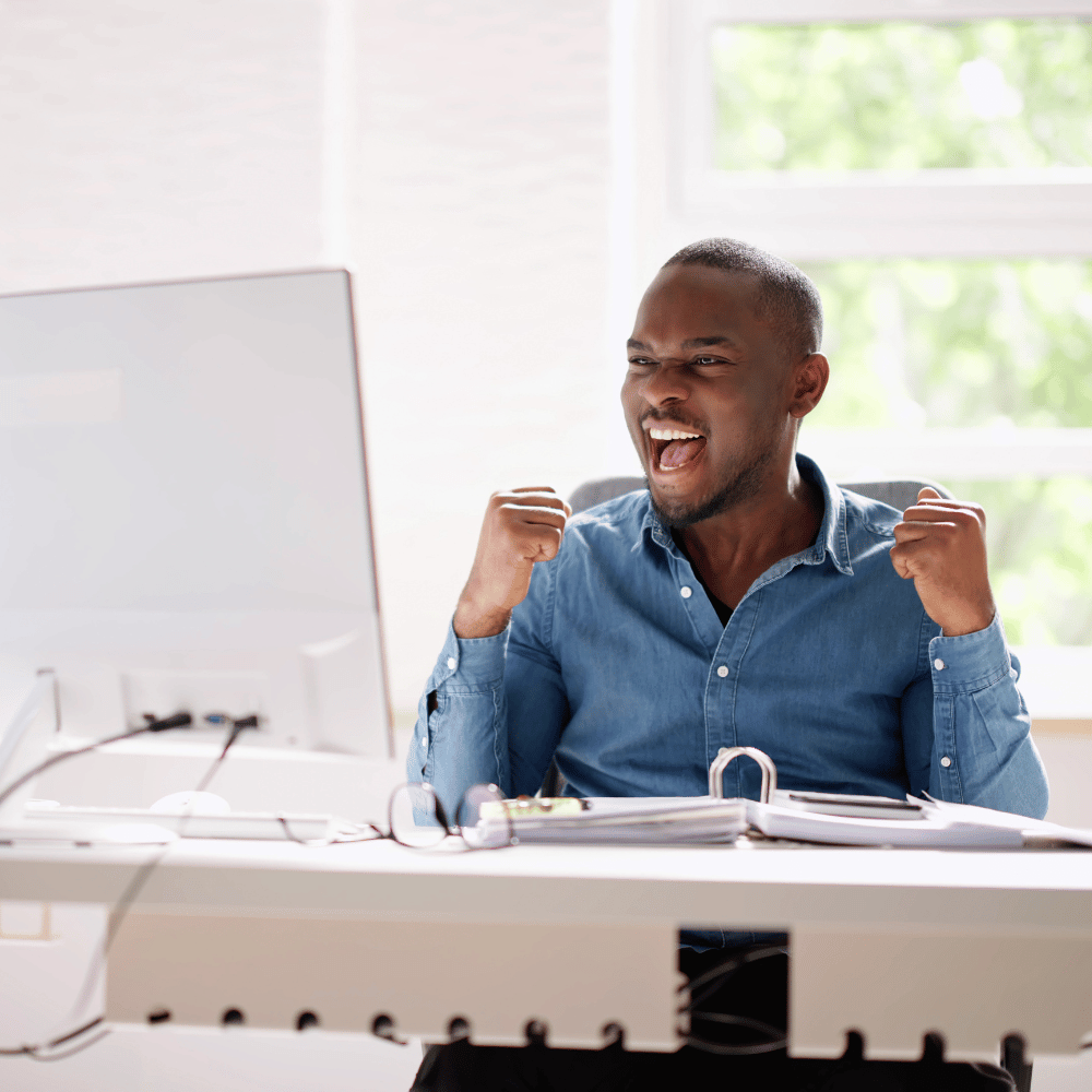 Person hebt im Büro beide Arme triumphierend nach oben und zeigt Freude über ein Ergebnis.