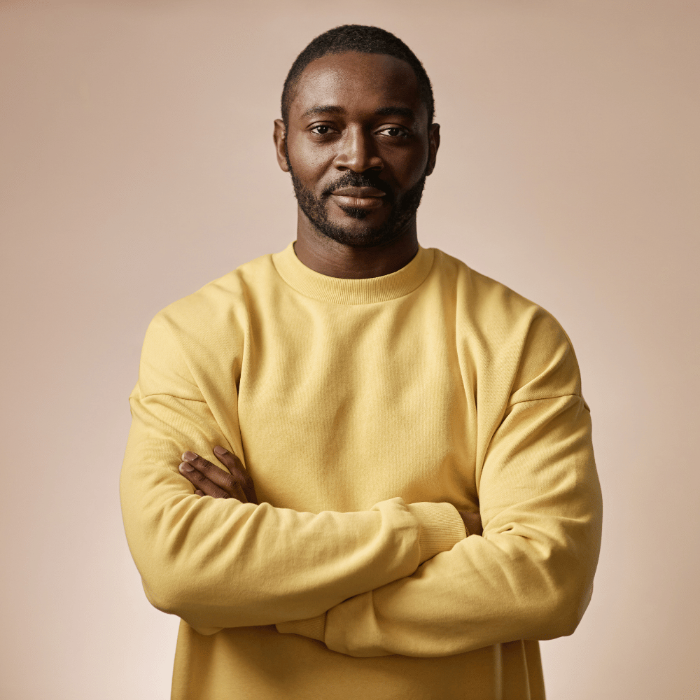 Selbstbewusste Person steht in gelbem Pullover und lächelt ruhig in die Kamera.